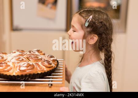 Kleines Mädchen bewundert frisch gebackene Zimtbrötchen Stockfoto