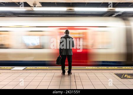 Älterer Passagier mit Laptoptasche, der vor dem Schnellzug auf dem U-Bahnsteig steht Stockfoto