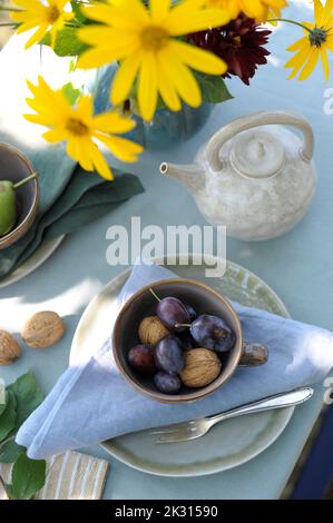 Teekannen, Vase mit blühenden Blumen, Pflaumen und Walnüssen auf herbstlich dekorierten Tisch Stockfoto