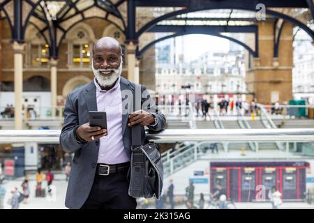 Lächelnder Passagier mit Mobiltelefon, das am Bahnhofsgeländer gelehnt ist Stockfoto