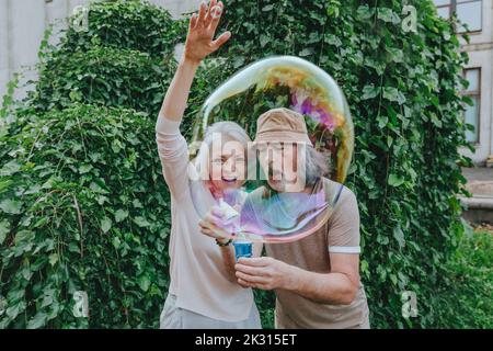 Glückliche reife Frau genießen von älteren Mann machen Blasen im Park Stockfoto