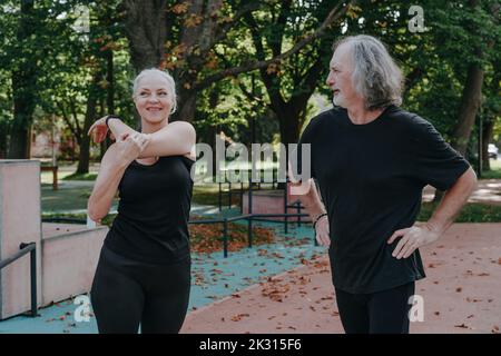 Reife Frau mit einem älteren Mann, der Stretching-Übungen im Park macht Stockfoto