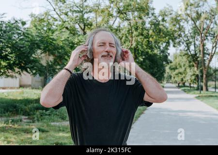 Lächelnder älterer Mann mit Kopfhörern, der im Park Musik genießt Stockfoto