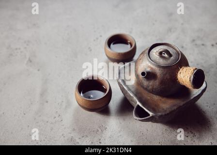 Eine antike Teekanne mit Keramikbechern auf grauem Hintergrund Stockfoto