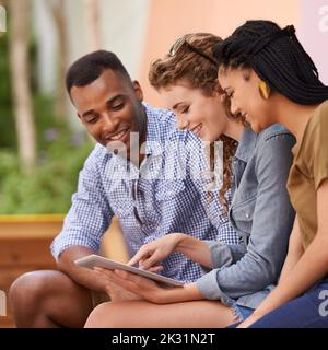 Willkommen bei den Wundern der E-Books. Drei Freunde lesen von einem digitalen Tablet, während sie draußen sitzen. Stockfoto
