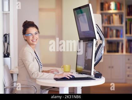 Meine Brille macht das Geschäft tragbar. Porträt einer jungen Frau, die eine intelligente Brille trägt, während sie an einem Computer mit zwei Bildschirmen arbeitet. Stockfoto