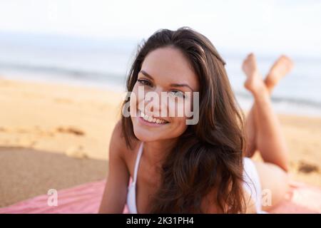 Die Zeit am Strand wird nie verschwendet. Beschnittenes Porträt einer schönen jungen Frau, die am Strand liegt. Stockfoto