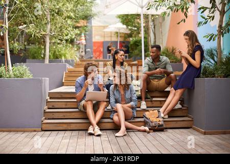 Chillen auf dem Campus zwischen den Klassen. Eine Aufnahme von Studenten, die auf dem Campus einen Laptop teilen. Stockfoto