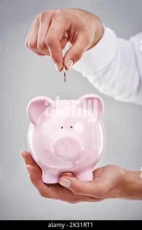 Jeden Cent sparen. Zugeschnittenes Bild eines Mannes, der Geld in ein Sparschwein gesteckt hat. Stockfoto