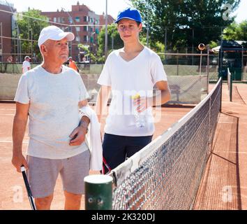 Großvater und Enkel sprechen auf dem Tennisplatz und spielen Tennis Stockfoto