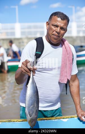 Angeln ist mein Leben. Porträt eines Fischers, der mit einem Fisch neben seinem Boot steht. Stockfoto