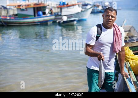 Angeln ist mein Leben. Porträt eines Fischers, der mit einem Fisch neben seinem Boot steht. Stockfoto