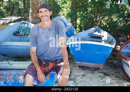 Angeln ist mein Leben. Porträt eines schroff aussehenden Fischers, der auf einem Fischerboot sitzt. Stockfoto