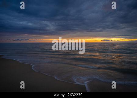 Ein Blick aus der Vogelperspektive auf den Strand, der sich während des Sonnenuntergangs über den Meereswellen ergießt Stockfoto