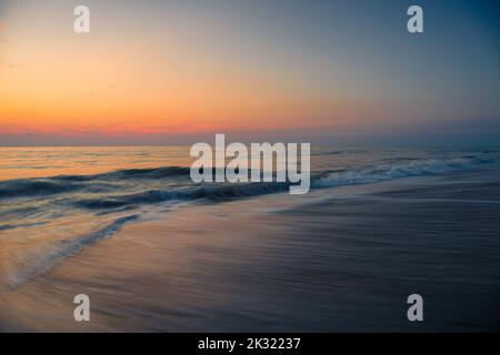 Ein Blick aus der Vogelperspektive auf den Strand, der sich während des Sonnenuntergangs über den Meereswellen ergießt Stockfoto