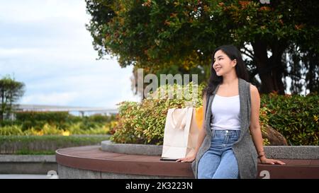 Schöne junge Frau sitzt auf der Bank im Park und bewundert schönen sonnigen Tag Stockfoto
