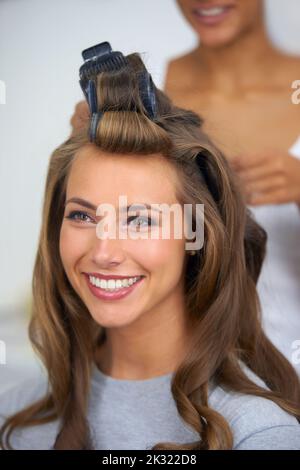 Sich einen Tag zu gönnen - Schönheitsbehandlung. Eine schöne junge Frau, die den Tag damit verbringt, ihre Haare und ihr Make-up zu machen. Stockfoto