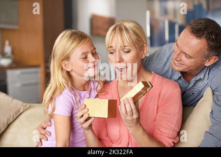 Familienfeste. Ein entzückendes kleines Mädchen, das ihrer Mutter ein Geburtstagsgeschenk gibt. Stockfoto