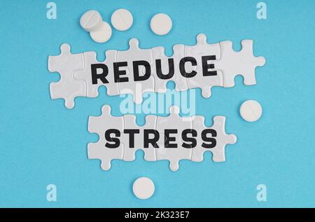 Medizinkonzept. Auf blauem Hintergrund Pillen und Puzzles mit der Aufschrift - REDUZIEREN STRESS Stockfoto