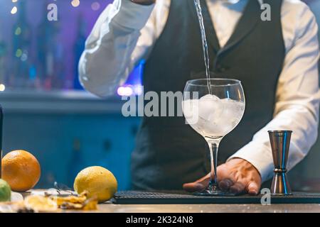 Ein unerkennbarer Barkeeper in einem weißen Hemd und einer schwarzen Schürze, der bei einer Party im Nachtclub einen Cocktail zubereitet. Nachtleben. Stockfoto