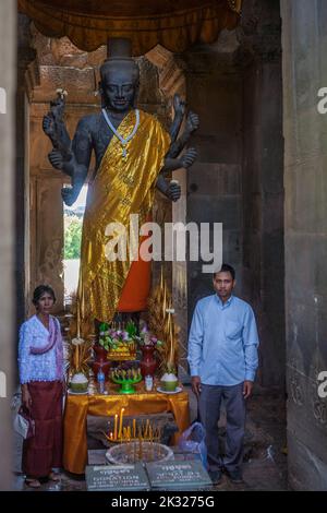 Zwei Gläubige stehen auf jeder Seite einer Statue von Vishnu, oder Ta Reach, im westlichen Gopura (Westtor) Eingang zu Angkor Wat, Siem Reap, Kambodscha Stockfoto