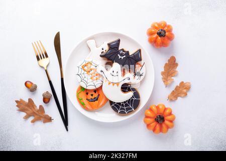 Halloween Tischgestellter mit Lebkuchen auf weißem Teller und kugelig auf weißem Hintergrund. Helle hausgemachte Kekse für Halloween-Party Stockfoto