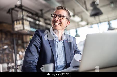 Unternehmer lächelt auf dem Computerbildschirm, während sie während einer Geschäftsreise in einem Vintage-Restaurant einen Kaffee trinken. Stockfoto