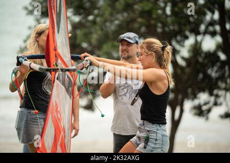 Zwei weibliche Teilnehmer stellen ihre Ausrüstung auf, um beim Waterbourne Watersports Festival am nationalen neuseeländischen Windsurf-Tragflächenboot-Rennen teilzunehmen Stockfoto