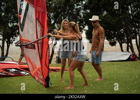 Zwei weibliche Teilnehmer stellen ihre Ausrüstung auf, um beim Waterbourne Watersports Festival am nationalen neuseeländischen Windsurf-Tragflächenboot-Rennen teilzunehmen Stockfoto