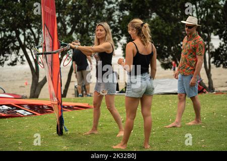 Zwei weibliche Teilnehmer stellen ihre Ausrüstung auf, um beim Waterbourne Watersports Festival am nationalen neuseeländischen Windsurf-Tragflächenboot-Rennen teilzunehmen Stockfoto