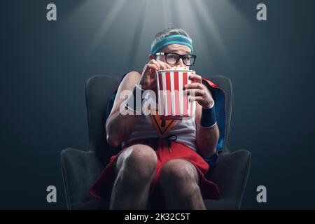 Lustiger Superheld, der Horrorfilme ansieht und Popcorn isst, ist erschrocken und versteckt sich Stockfoto