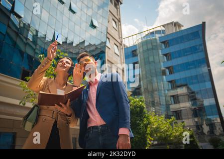 Junge männliche und weibliche Geschäftsleute zeigen irgendwo hin und lächeln darüber Stockfoto