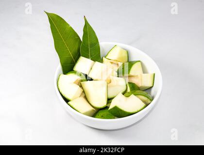 Eine Schale roher grüner Mangos mit Mango-Blättern, isoliert auf weißem Hintergrund. Stockfoto