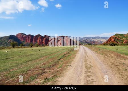 Schotterstraße zwischen ungewöhnlichen Felsformationen aus rotem Sandstein in der Schlucht Sieben Bullen in Jeti-Oguz, Kirgisien Stockfoto