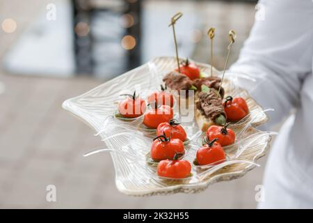 Der Kellner hält ein Tablett mit appetitlichen Snacks bereit, die der Form von Tomaten nachempfunden sind Stockfoto