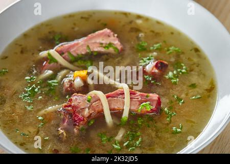Suppe aus geräucherten Rippchen mit Gemüse und Kräutern in einer weißen Schüssel - Nahaufnahme Stockfoto