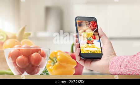 Frau, die in ihrer Küche eine Mahlzeit zubereitet, sucht mit ihrem Smartphone POV shot in einer Koch-App nach gesunden Rezepten Stockfoto