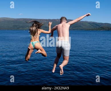 Die Menschen genießen den Sommer in Luss am Loch Lomond, Schottland, beim Springen und Schwimmen im kalten, frischen Wasser des loch. Stockfoto