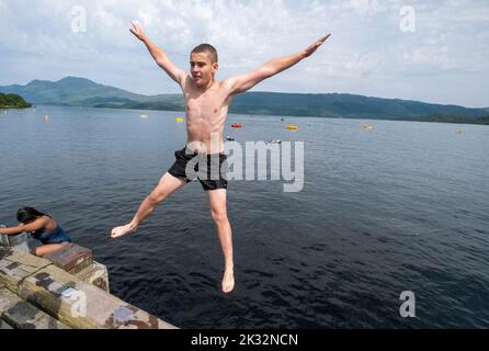 Die Menschen genießen den Sommer in Luss am Loch Lomond, Schottland, beim Springen und Schwimmen im kalten, frischen Wasser des loch. Stockfoto