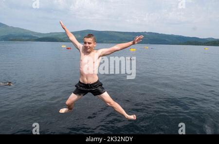 Die Menschen genießen den Sommer in Luss am Loch Lomond, Schottland, beim Springen und Schwimmen im kalten, frischen Wasser des loch. Stockfoto