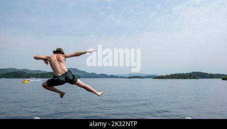 Die Menschen genießen den Sommer in Luss am Loch Lomond, Schottland, beim Springen und Schwimmen im kalten, frischen Wasser des loch. Stockfoto