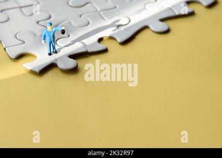 Einzelne kleine Arbeiter Miniatur-Figur am Rand des verbundenen Puzzle. Gelber Papierhintergrund, langer Schatten. Konzept Hintergrund mit Copy-Space, Ort Stockfoto