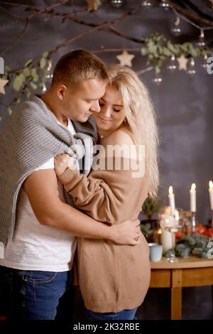 Schönes Paar in Liebe zu Mann und blonde Frau in ästhetischen gemütlichen Wohnräumen mit festlichen Tisch-Einstellung. Ehrlicher, wahrer Moment. Gute Laune und gute Laune Stockfoto