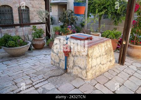 Jerusalem, Israel - 7.. Juli 2022: Ein alter Brunnen in einem gepflasterten Hof eines historischen Hauses. Stockfoto