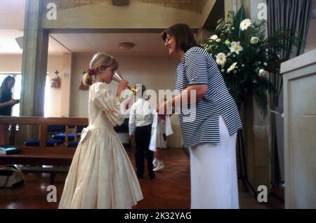 Mädchen trinkt geweihten Wein aus Kelch bei der ersten Kommunion St. Bernard's Church Lingfield Surrey England Stockfoto