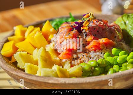 Thunfisch und Lachs Poke Bowl Roher Fischsalat Asiatische Speisen mit Bohnen, Edamame, Quinoa, Avocado, Ananas, Gurke und Salat in einer Schüssel - Nahaufnahme Stockfoto