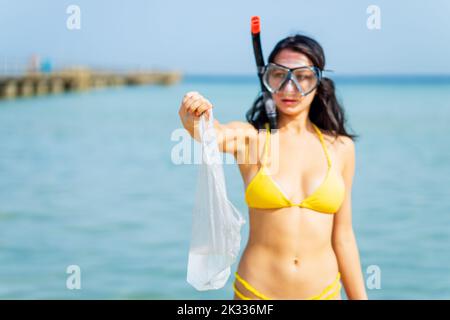 Frau in gelbem Bikini und Scuba, die einen Plastikmüll aus dem Meer holt Stockfoto