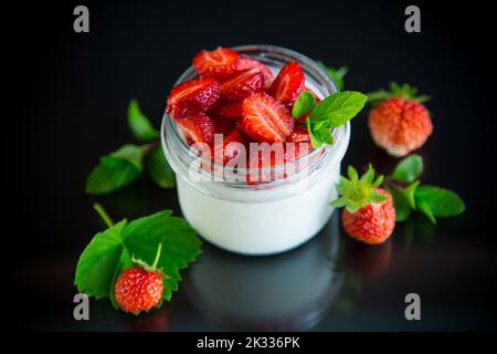Süßer hausgemachter Joghurt mit frischen reifen Erdbeeren in einem Glasglas isoliert auf schwarzem Hintergrund Stockfoto