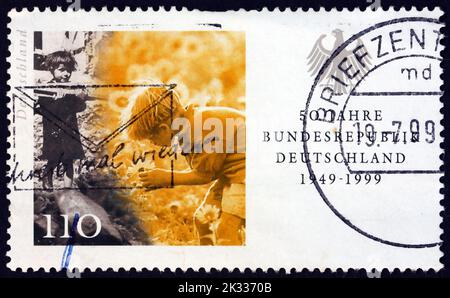 DEUTSCHLAND - UM 1999: Eine in Deutschland gedruckte Briefmarke zeigt das Holz tragende Kind und das Blumen pflücken, Szenen aus den Jahren 1949 und 1959, 50. Jahre Fe Stockfoto