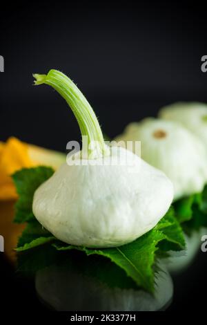 Frischer Bio-Kürbis mit Blumen und Laub isoliert auf schwarzem Hintergrund Stockfoto